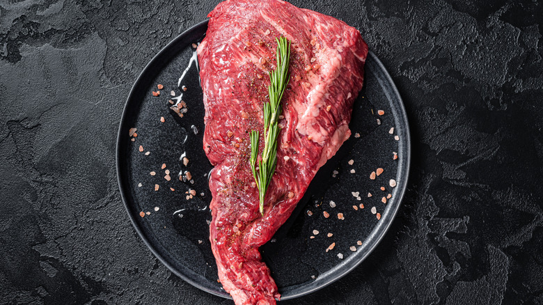 A raw tri-tip steak seasoned with salt and rosemary