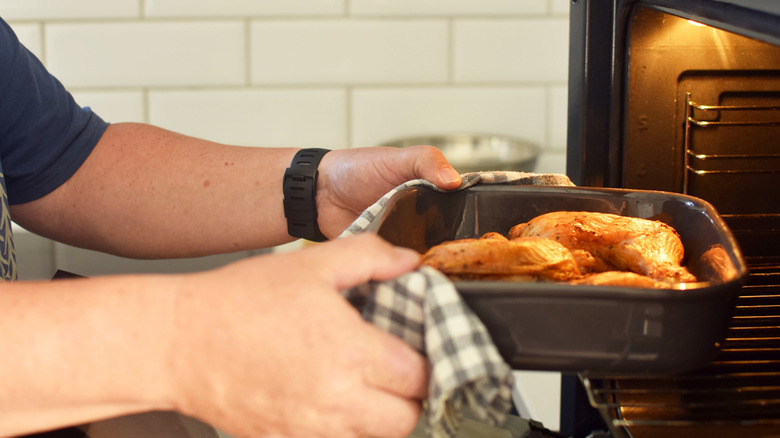 A person taking chicken thighs out of the oven