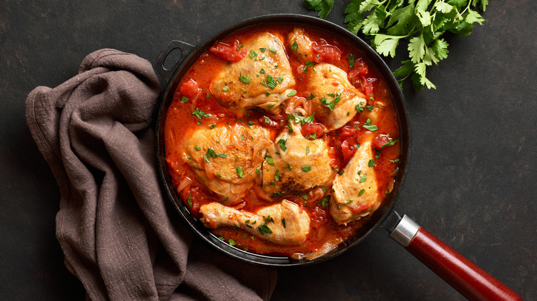 Tomato sauce around chicken legs and thighs in a pan