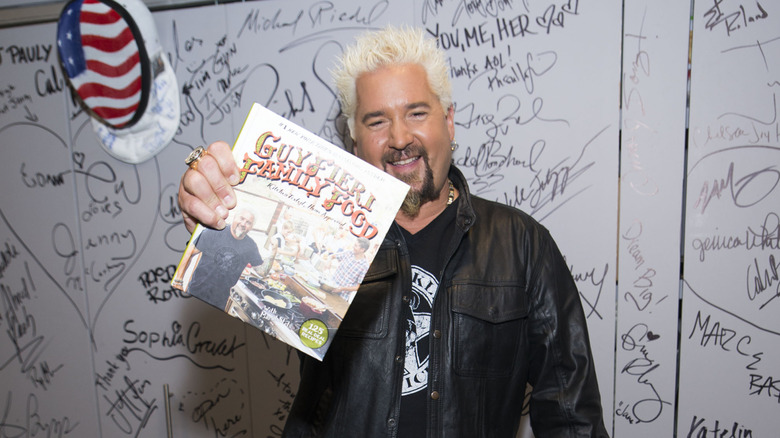 Guy Fieri holding a copy of his cookbook Guy Fieri Family Food