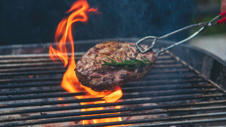 meat held by tongs over a charcoal grill outside