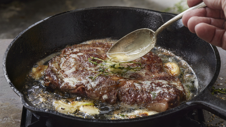 a rib eye steak in a hot black pan with butter being spooned over it