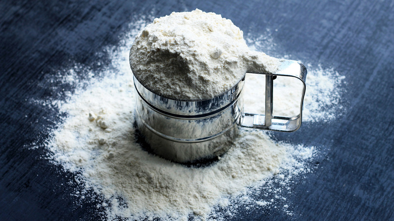 silver mug sieve full of flour, sitting on a dark background