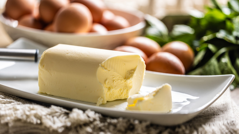 a block of butter sitting on a white dish in the foreground, with a bowl of eggs in the background