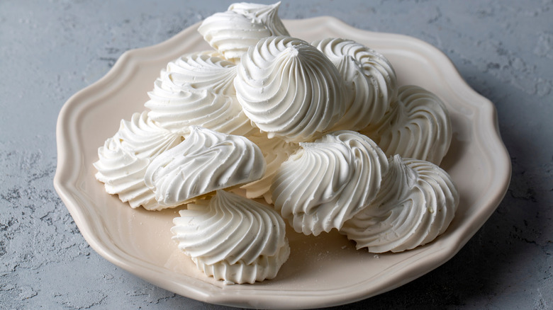 a shallow beige bowl of white, piped meringue swirls on a grey surface