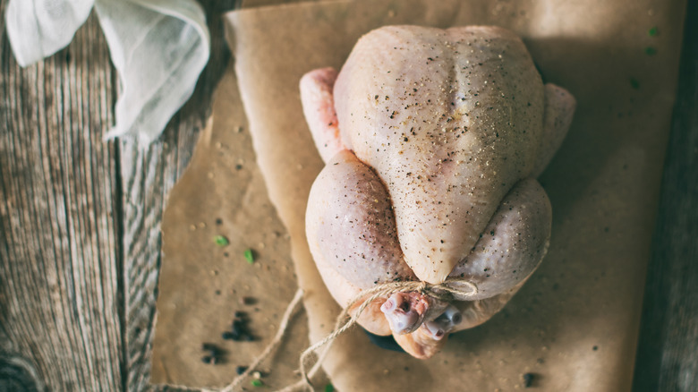 a trussed chicken, tied at the ends of its legs, on brown paper, on a wooden surface