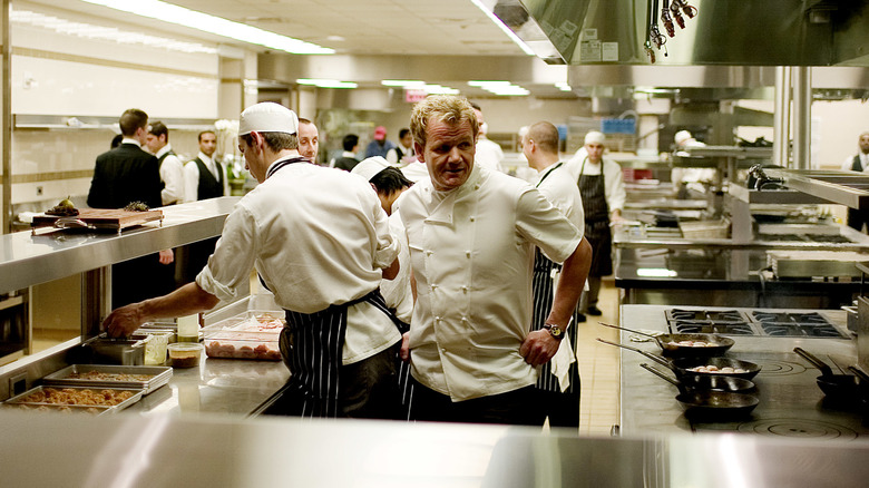 chef Gordon Ramsay wearing chef's whites and standing in a busy hotel kitchen