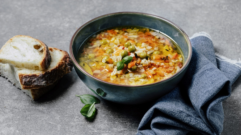 a bowl of vegetable soup between three slices of rustic bread and a grey napkin