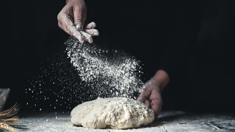 Hands sprinkling flour on bread dough