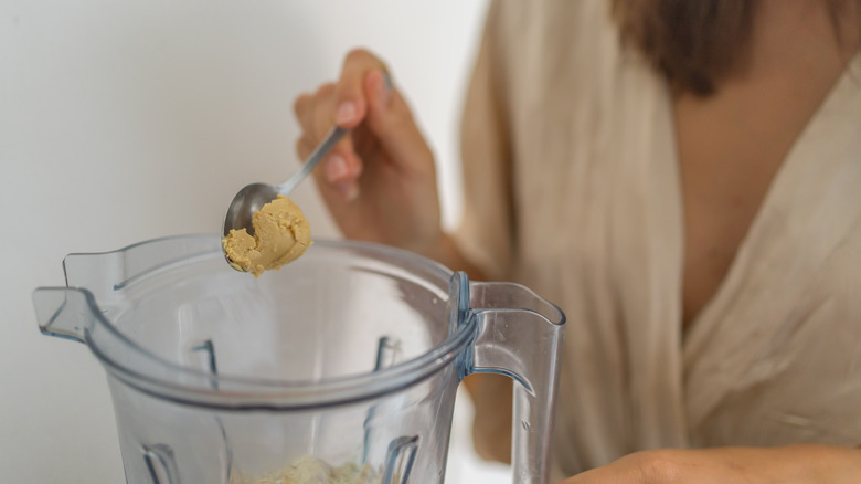 A woman adds a spoonful of tahini to a blender