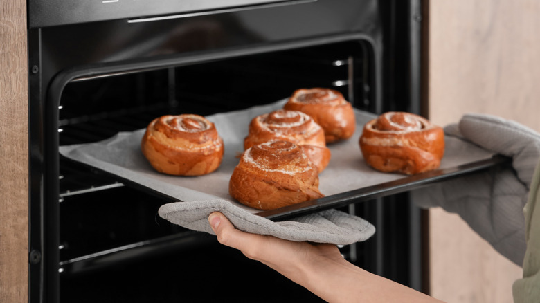 A person taking a tray of cinnamon rolls out of the oven