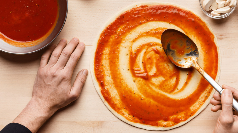 man putting pizza sauce dough