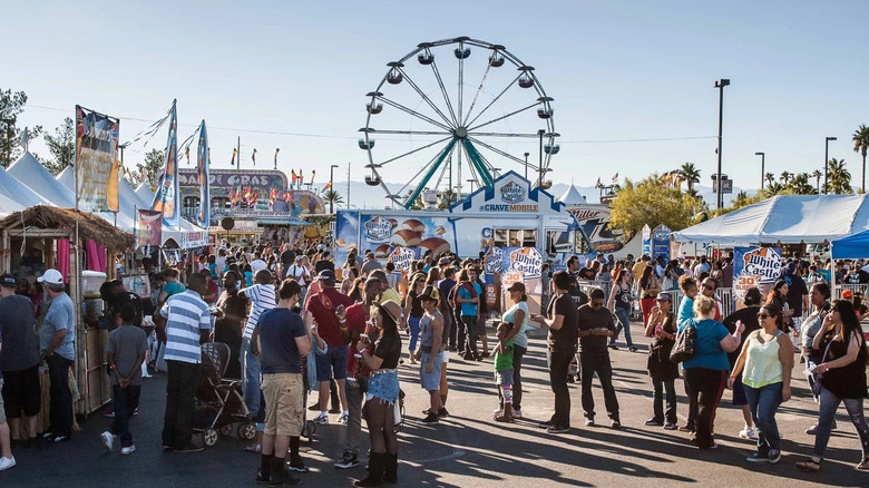 crowd of people waiting in line for food with Ferris wheel in background