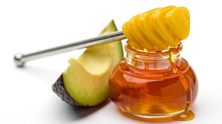 a slice of avocado next to a glass jar of honey that has a honey dipper leaning on it