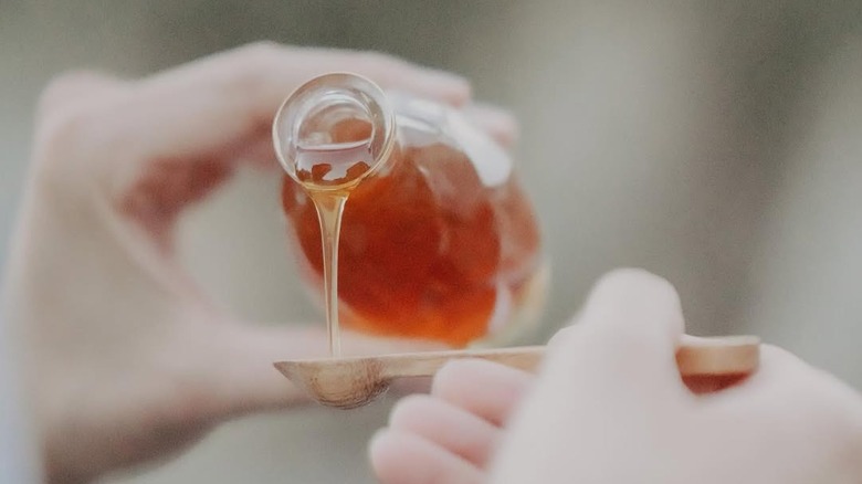 a small jar of Elvish honey being poured onto a wooden spoon