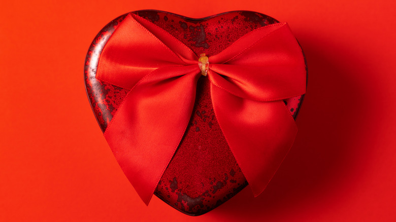 A dark red chocolate heart with a scarlet ribbon on top, sitting on a scarlet background