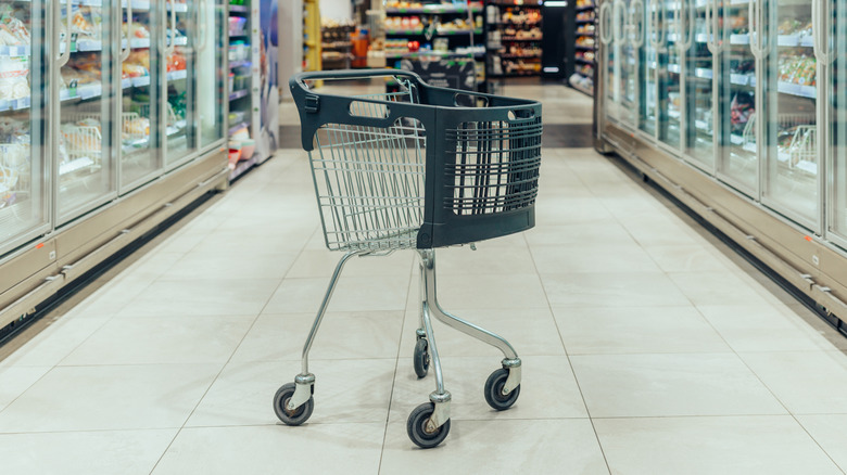 an empty shopping cart standing in the freezer aisle of a supermarket