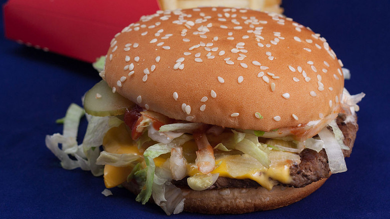 a close-up of a McDonald's Big N' Tasty burger on a blue background, with a box of fries in the background