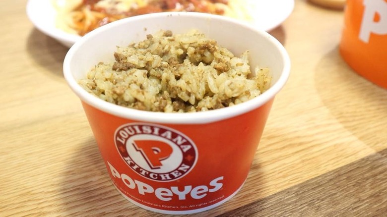 A close-up of a pot of Popeyes Cajun rice on a wooden table