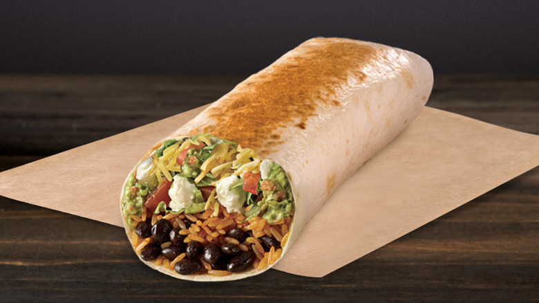 a close-up of a 7 layer burrito on a brown piece of paper, sitting on a table