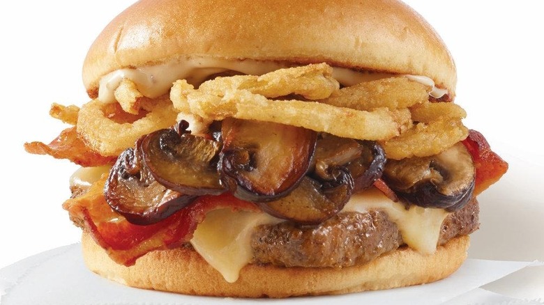 a close-up of a Wendy's smoky mushroom bacon cheeseburger on a white background