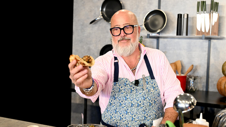 Andrew Zimmern on cooking set holding a pancake