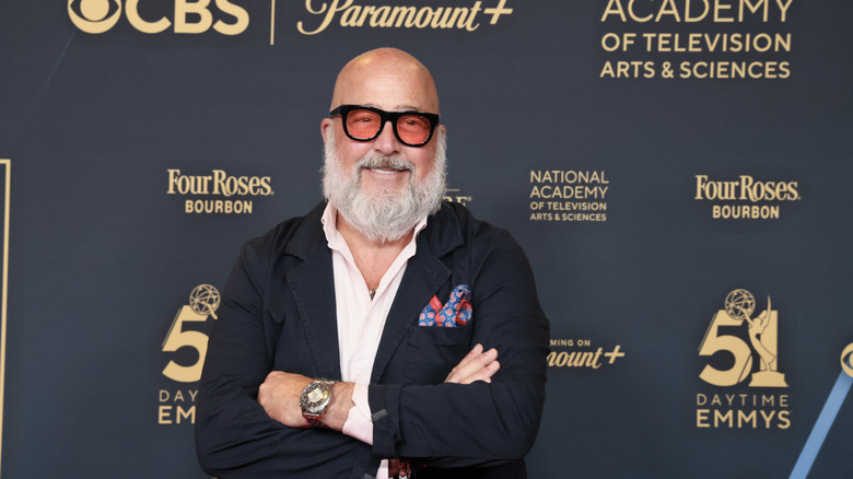 Andrew Zimmern smiling in front of a step and repeat