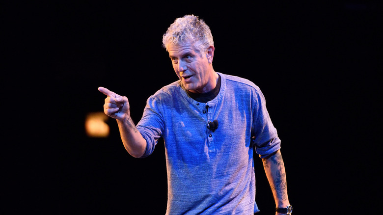 Anthony Bourdain in blue shirt and pointing on stage