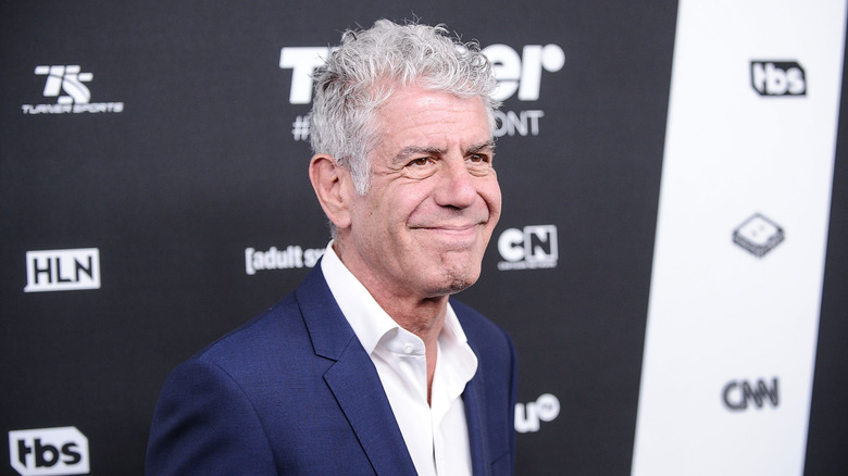 Anthony Bourdain smiling in front of step and repeat