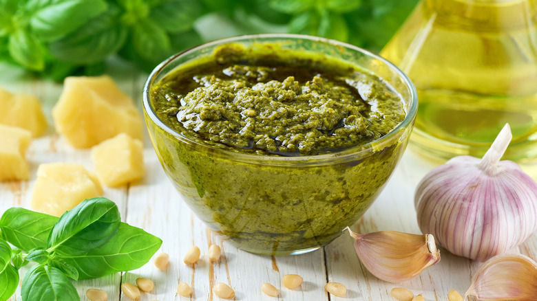 A dish of pesto surrounded by onions, garlic, basil, and olive oil