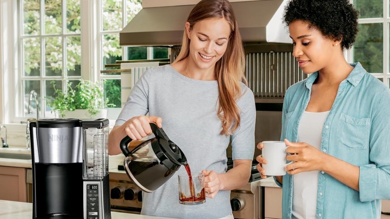 Two people pouring coffee from a Ninja coffee brewer