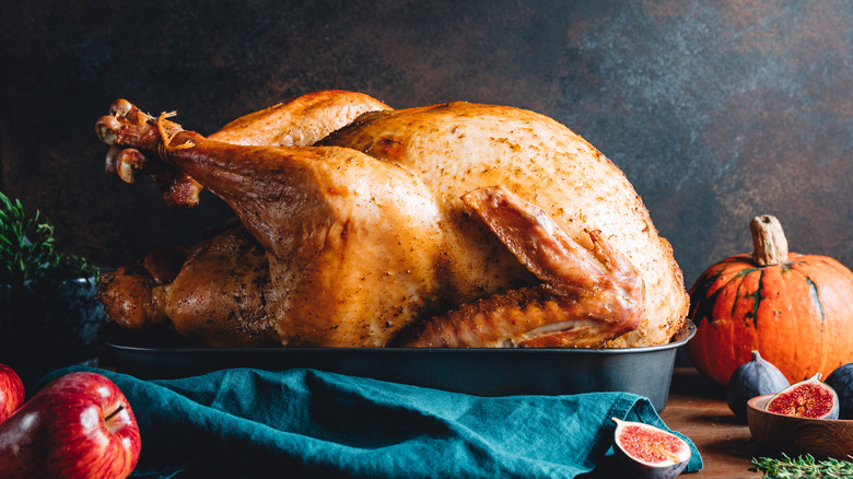 cooked turkey in serving dish with pumpkin, apples and fig