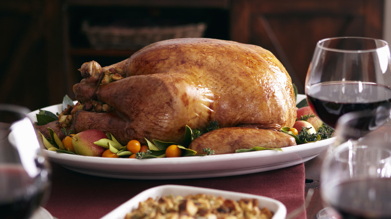 cooked whole turkey on a table with sides and wine glasses