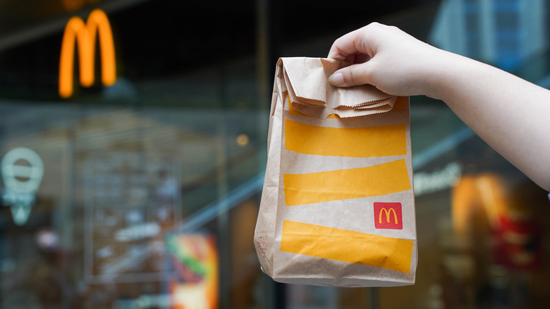 Hand holding up McDonald's-branded paper bag in front of store facade.