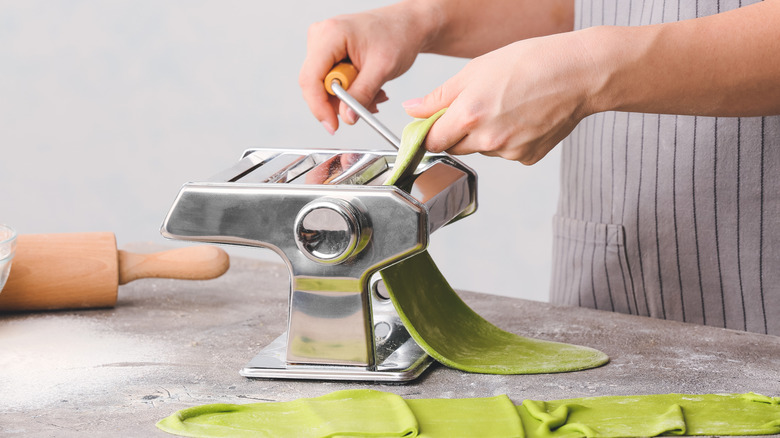 Rolling spinach pasta through a pasta machine.