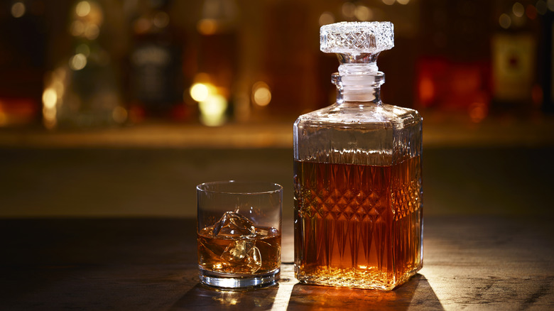 Bourbon decanter and glass with bourbon on wood table.