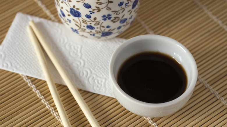 A bowl of soy sauce next to chopsticks