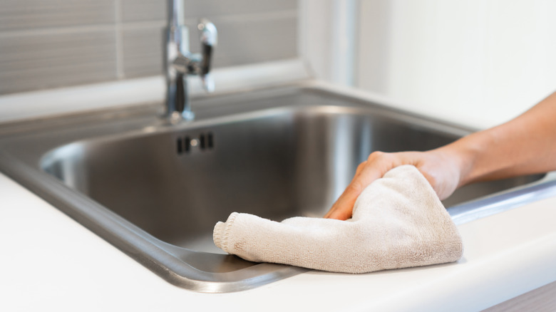 Person wiping stainless steel sink with cloth