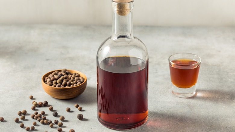 Brown liquid in a bottle near a wooden bowl of allspice