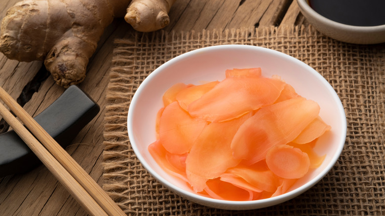 A bowl of pickled ginger root next to fresh ginger root