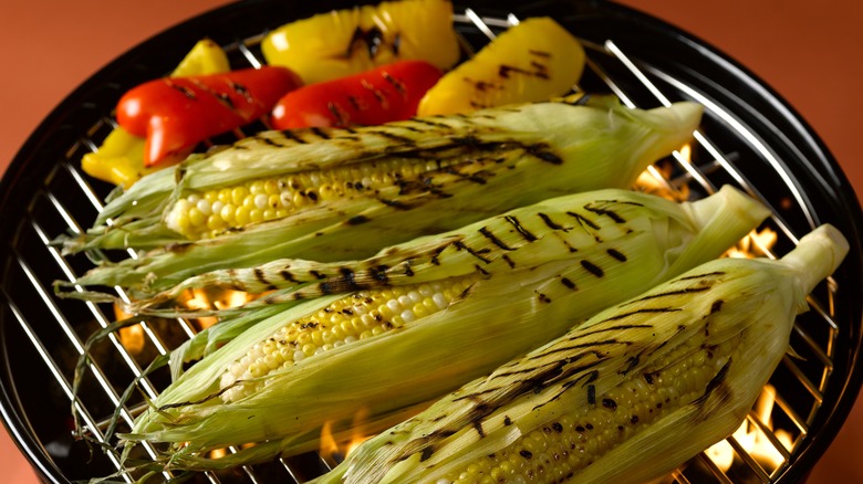 Peppers and unhusked corn on a grill