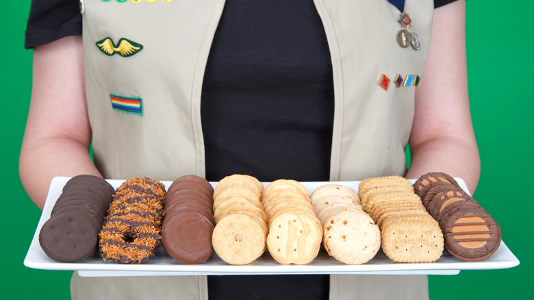 A Cadette level Girl Scout holding a tray of cookies.