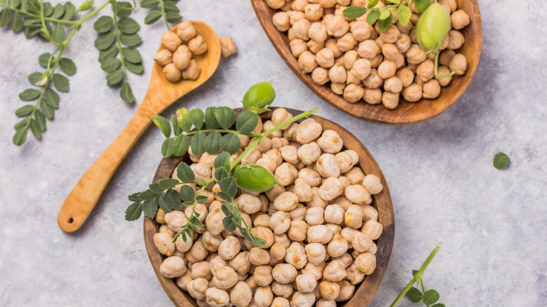 raw green chickpea shells atop wooden bowls of dried chickpeas