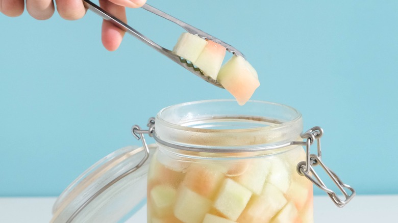 tong taking three cubes of pickled watermelon rind out of a jar