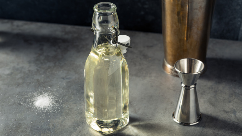 Homemade sugar simple syrup in bottle next to cocktail jigger and shaker.