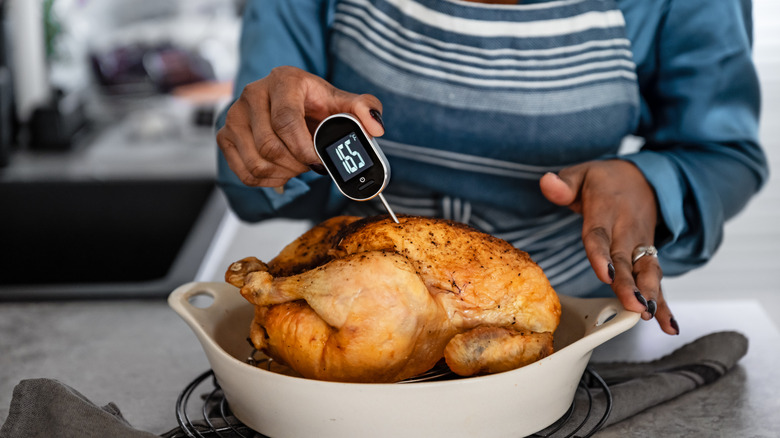 A woman uses a meat thermometer on a roast chicken