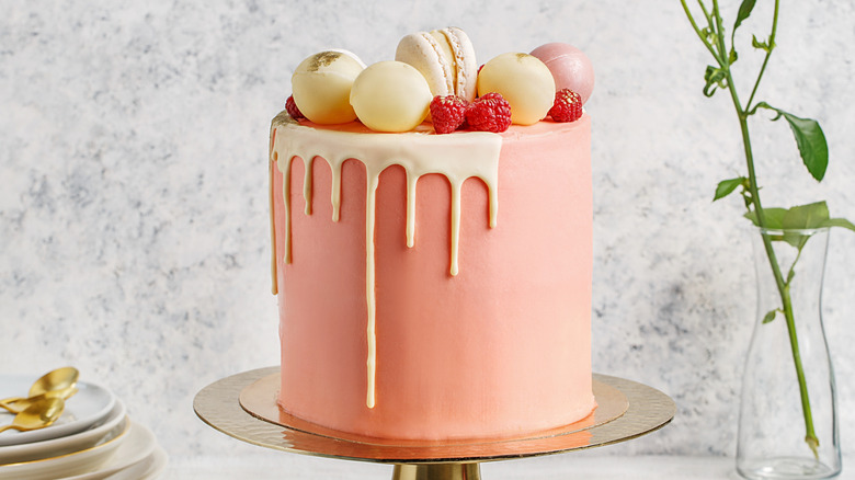 Tall pink cake with macaroons, raspberries, and chocolate balls on golden stand