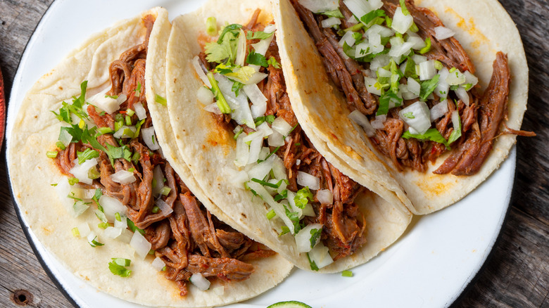 Three beef barbacoa tacos on white plate closeup