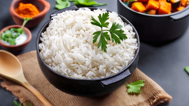 Cooked white rice in an iron pot dressed beside a wooden spoon.