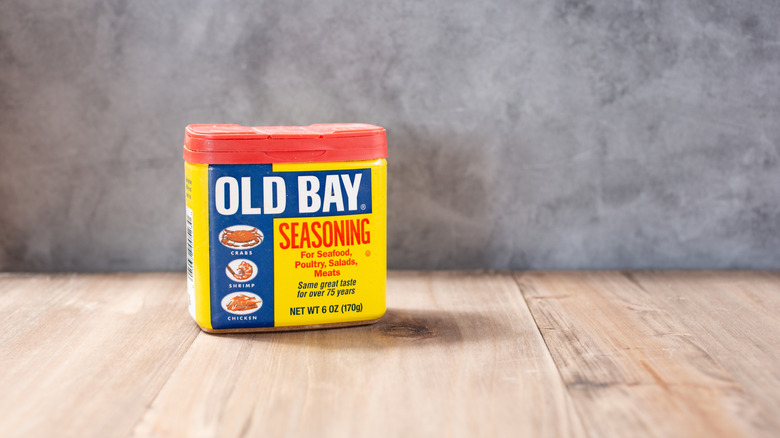 Old Bay seasoning container on wood surface, neutral gray background.